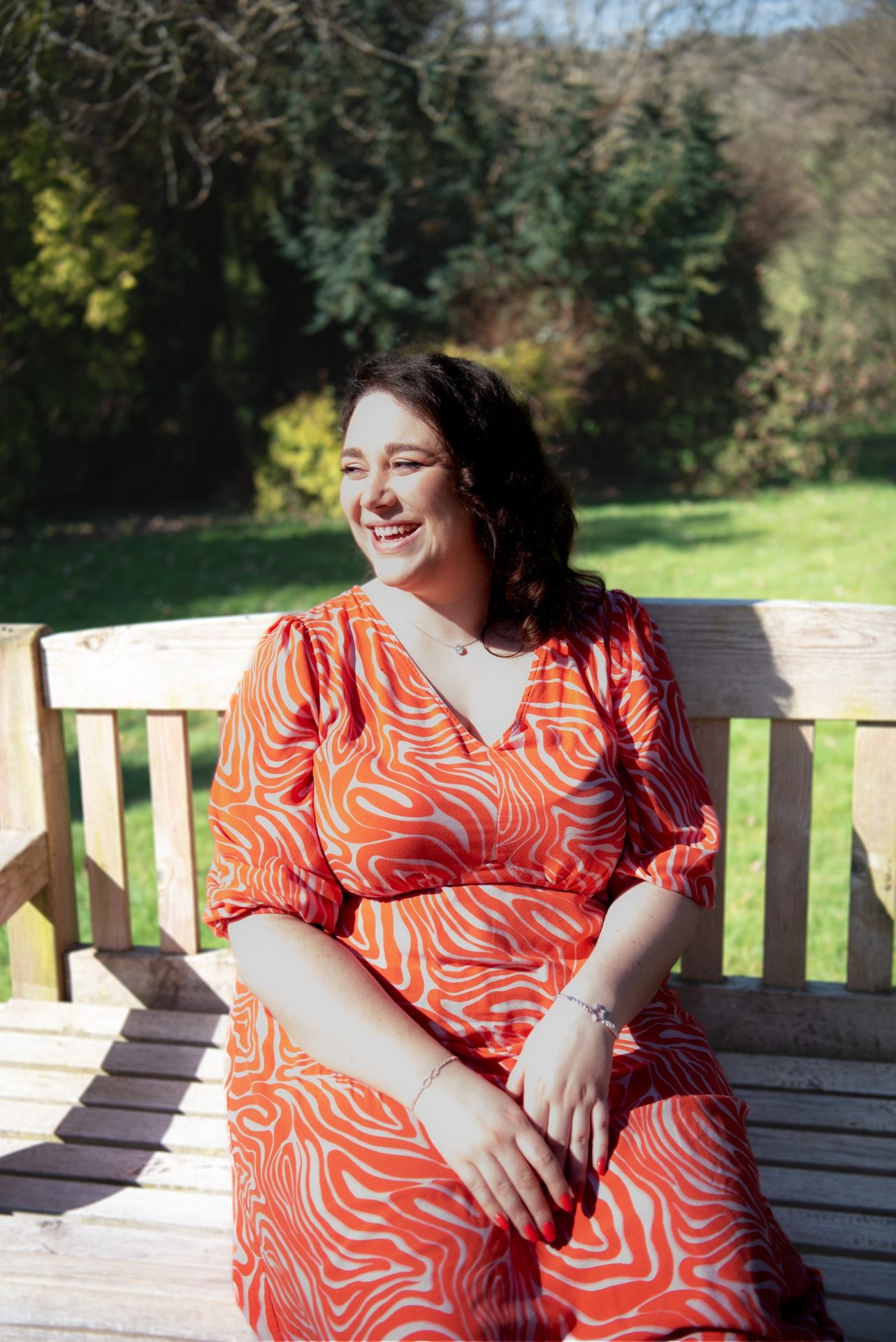 Madi Kish, Inspired To Change hypnotherapist in Tunbridge Wells, smiling on a wooden garden bench in the sunshine.
