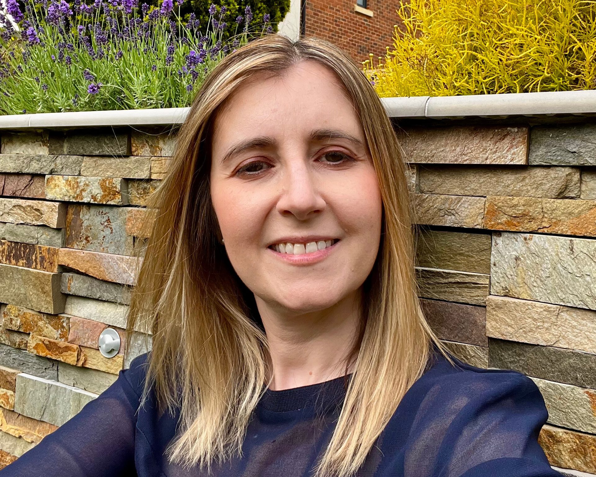 Marina Love, Inspired To Change hypnotherapist near Aylesbury, smiling in front of a stone garden wall and lavender.