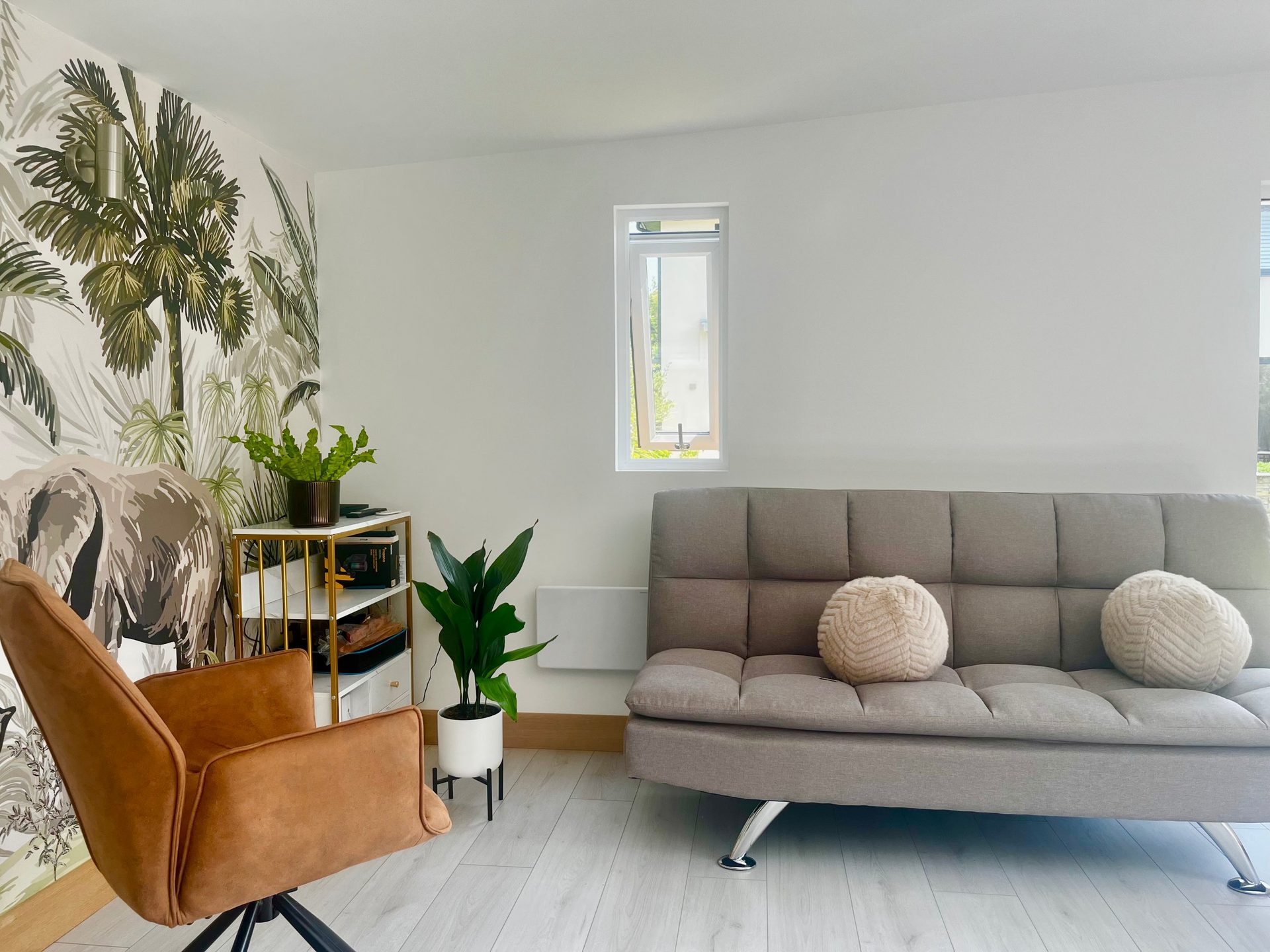 Bright therapy room with a tan armchair, grey sofa, plants and jungle wallpaper at Marina Love’s practice near Aylesbury.