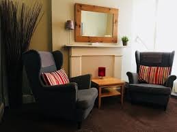 Two grey wingback chairs either side of a fireplace in the therapy room where Peter Ely sees clients in Islington.