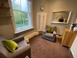 Therapy room with grey armchairs and a large sash window at Peter Ely’s practice in Islington.