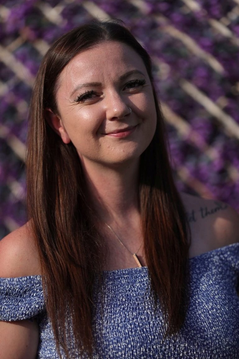 Samantha Morson, hypnotherapist in Canvey Island, smiling in the sunshine in front of a purple floral wall.